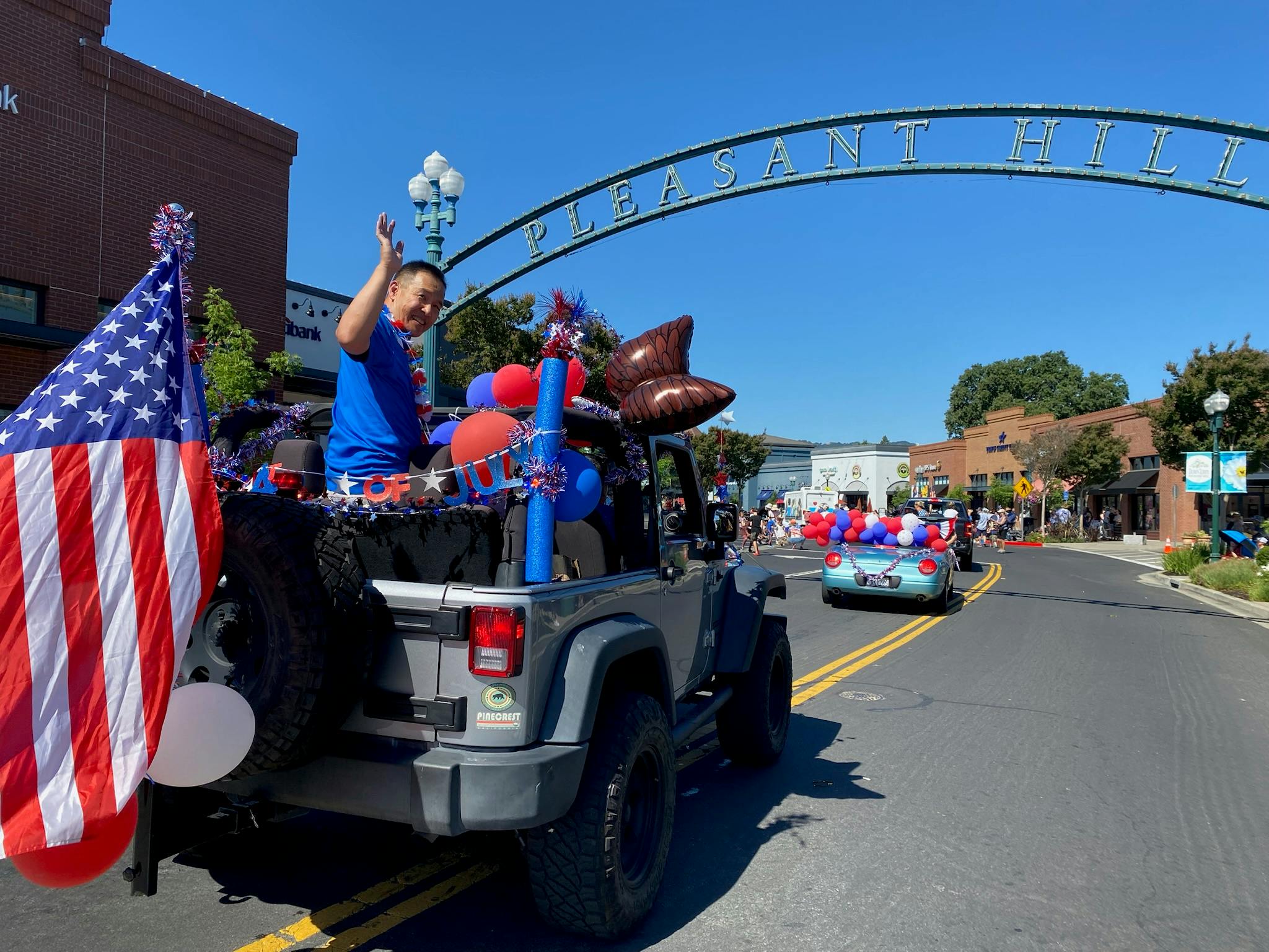 Candidate Dr. Quy Tran riding the back of a jeep in a parade for Fourth of July in Pleasant Hill