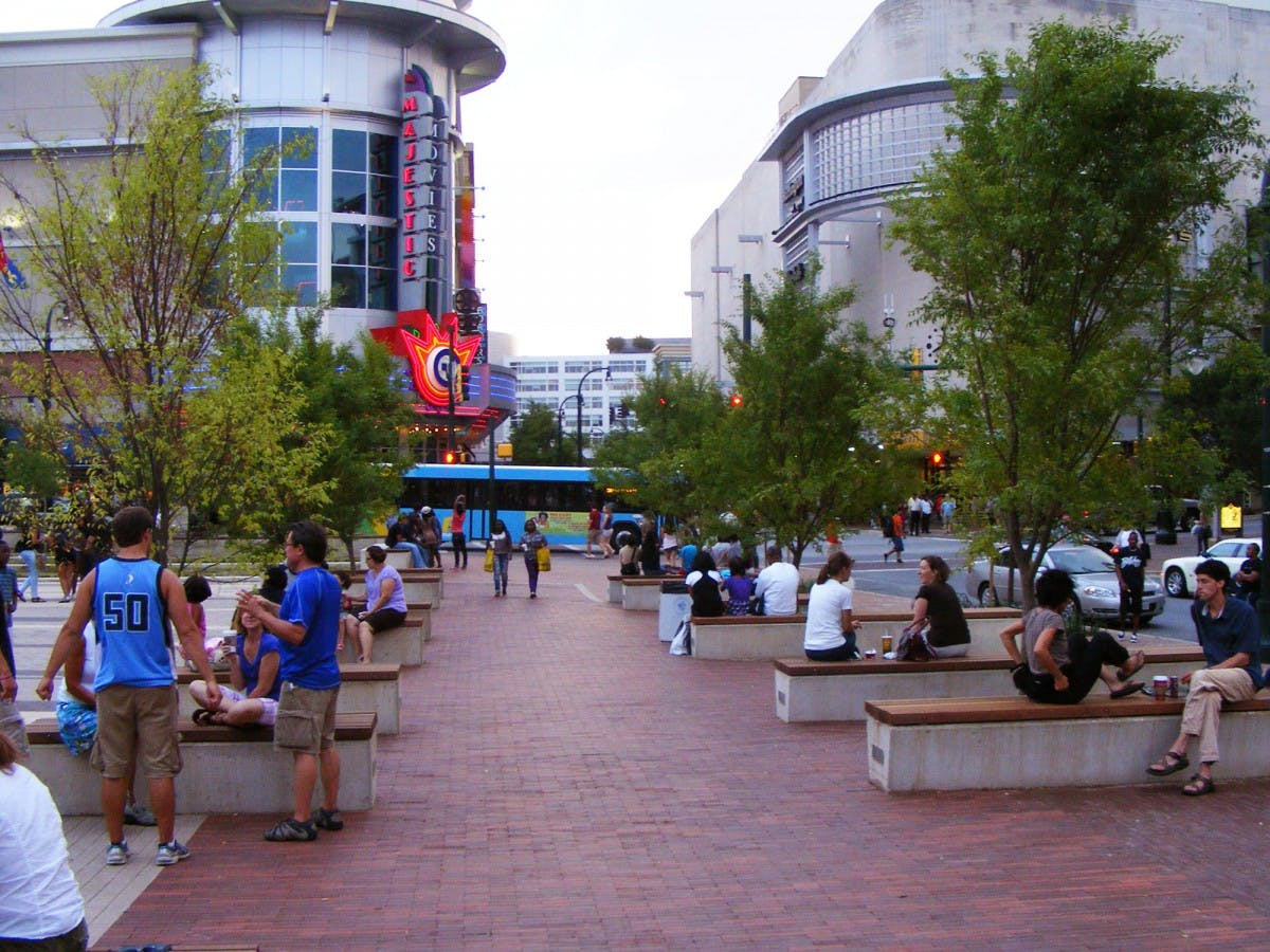 Image of city with people walking and sitting on benches, with a bus in the background and a theater sign