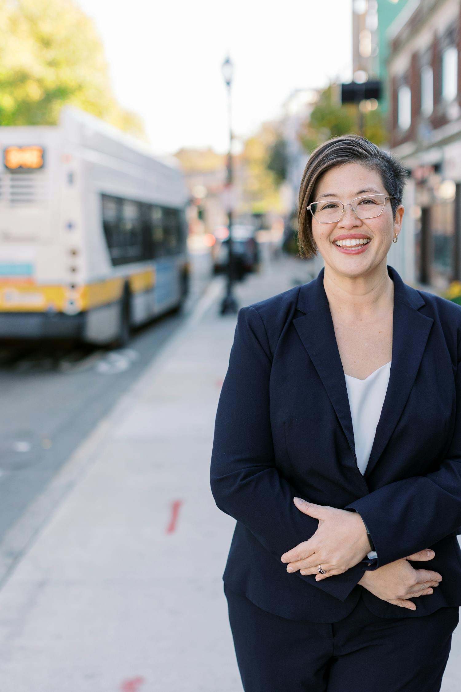 Persis Yu on a Roslindale sidewalk with an MBTA bus in the background