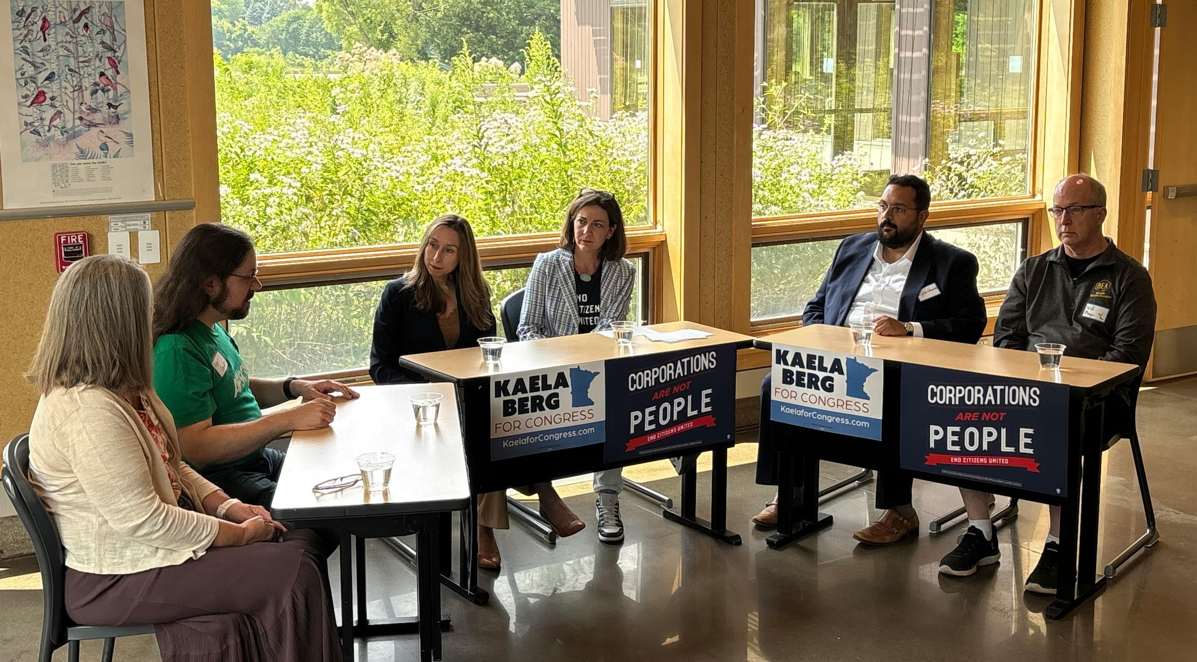 Speakers at roundtable in Twin Cities, seated at tables in a circle. State Representative Kaela Berg and Tiffany Muller are seated in the center. Kaela Berg for Congress and End Citizens United decorate the tables. 