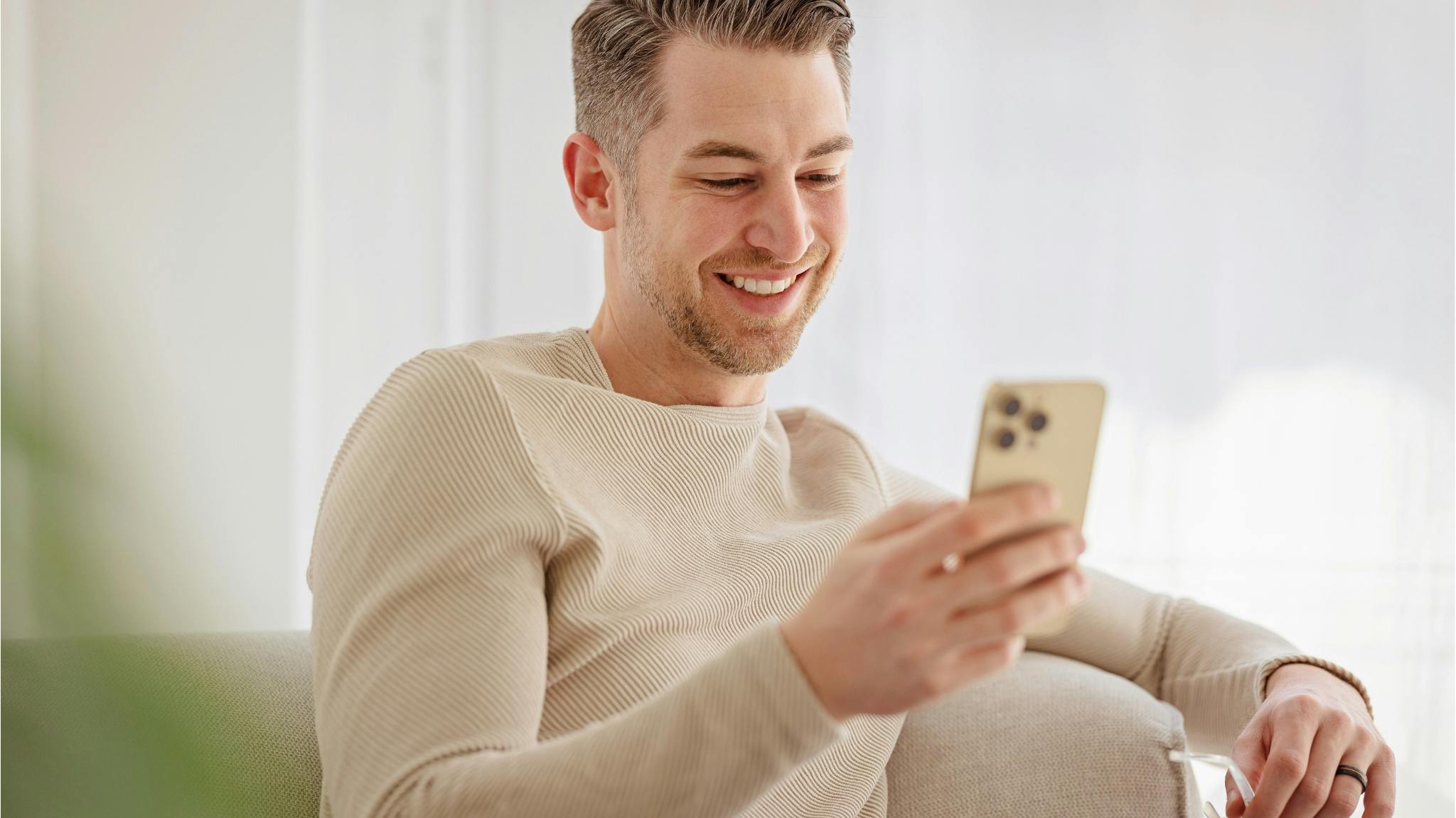 A smiling man relaxing on a couch, looking at his phone