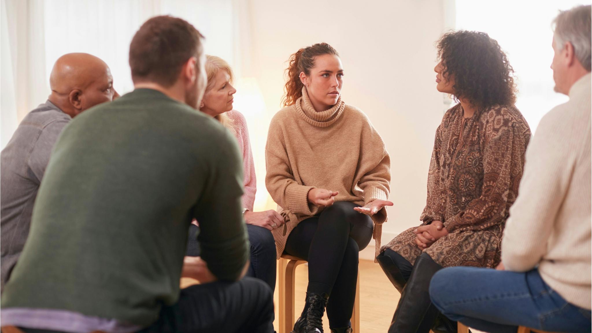 A diverse group of adults sitting in a circle, talking together, as one woman gestures while speaking.