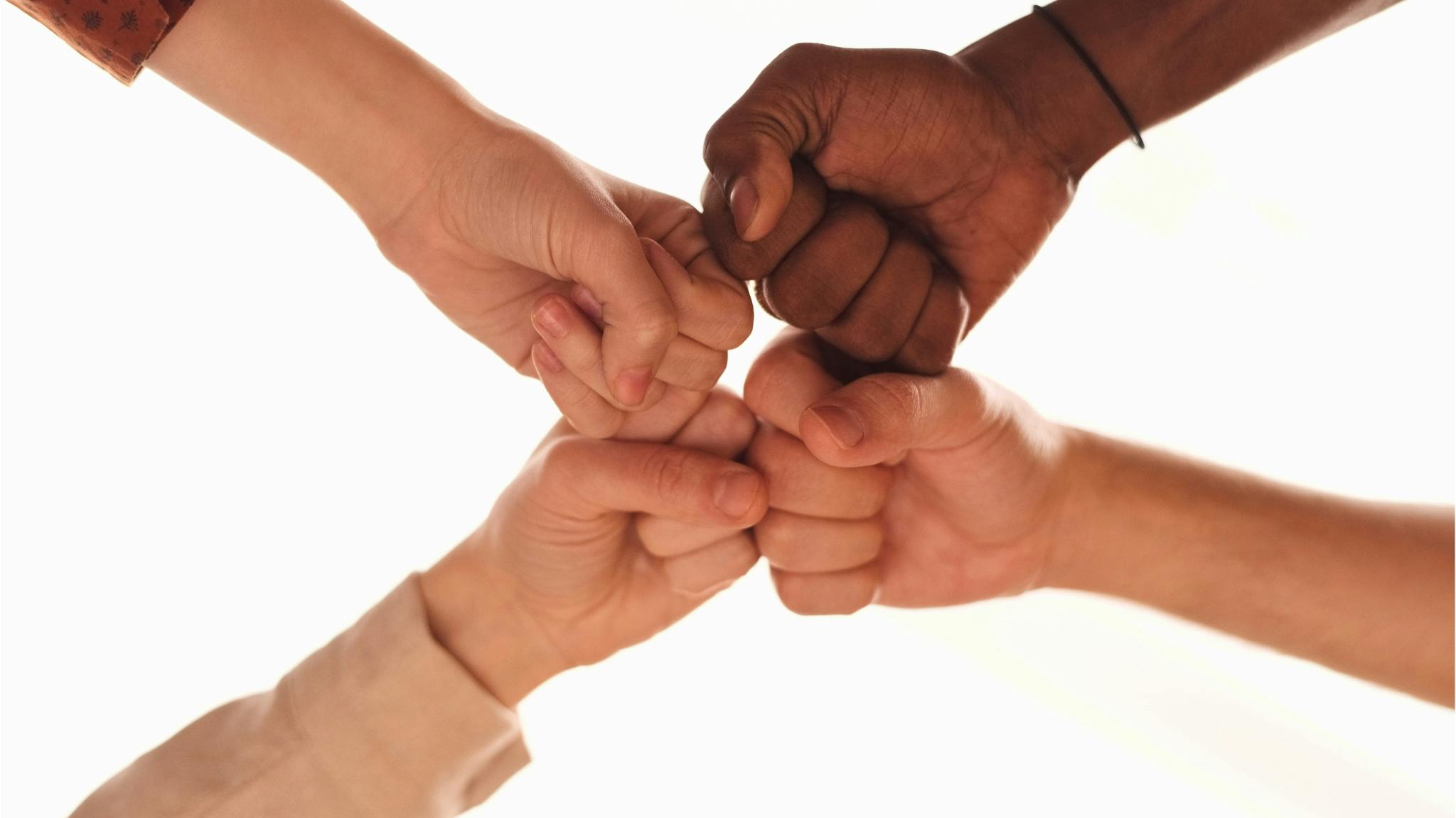 Four people of different skin tones joining their fists together in the center of a circle