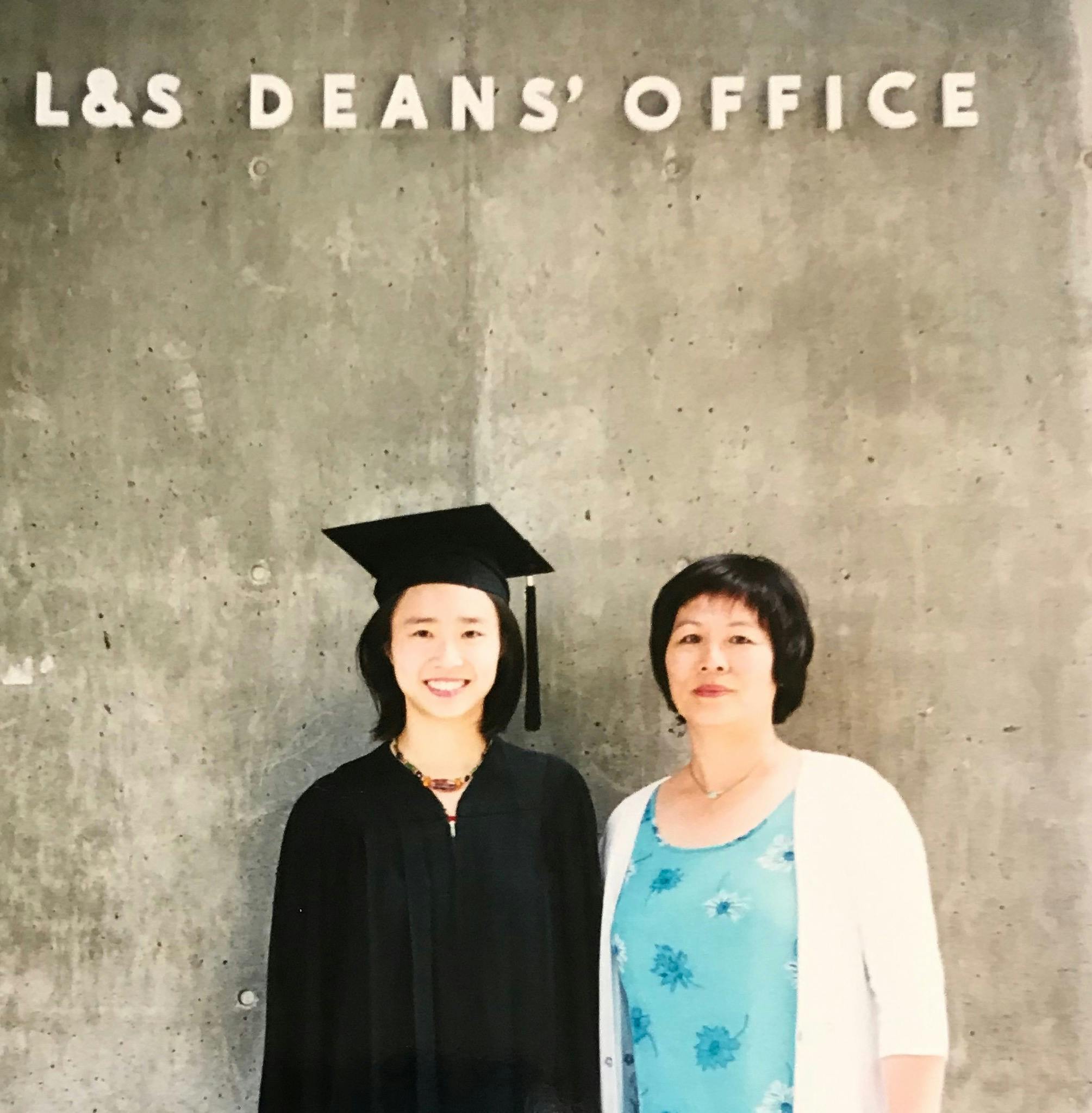Connie Chan candidate for Congress in a graduation cap and gown smiling beside a family member in front of a building