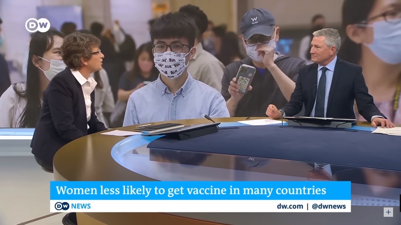 Nina in a DW tv interview, at the background can be seen people with disposable facemasks