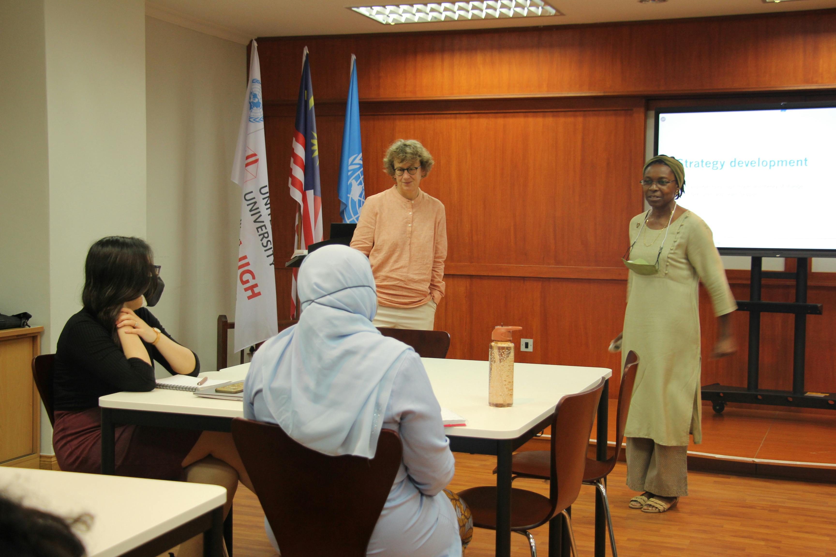 Photo of Nina in a meeting, a UN flag can be spotted at the background of the meeting room