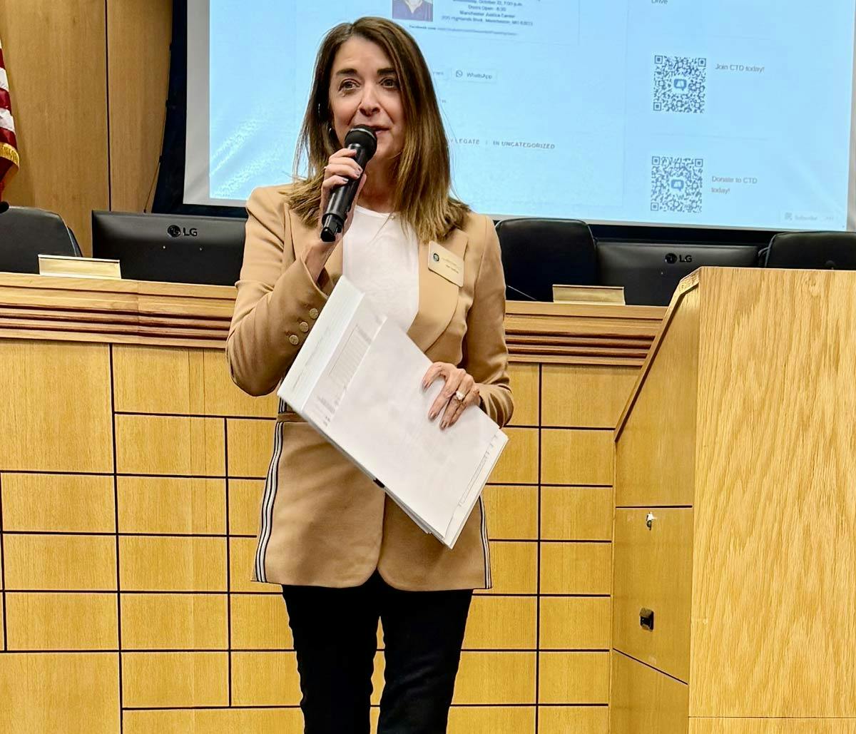 Photo of Joan VonDras, microphone in had, addressing a group of people