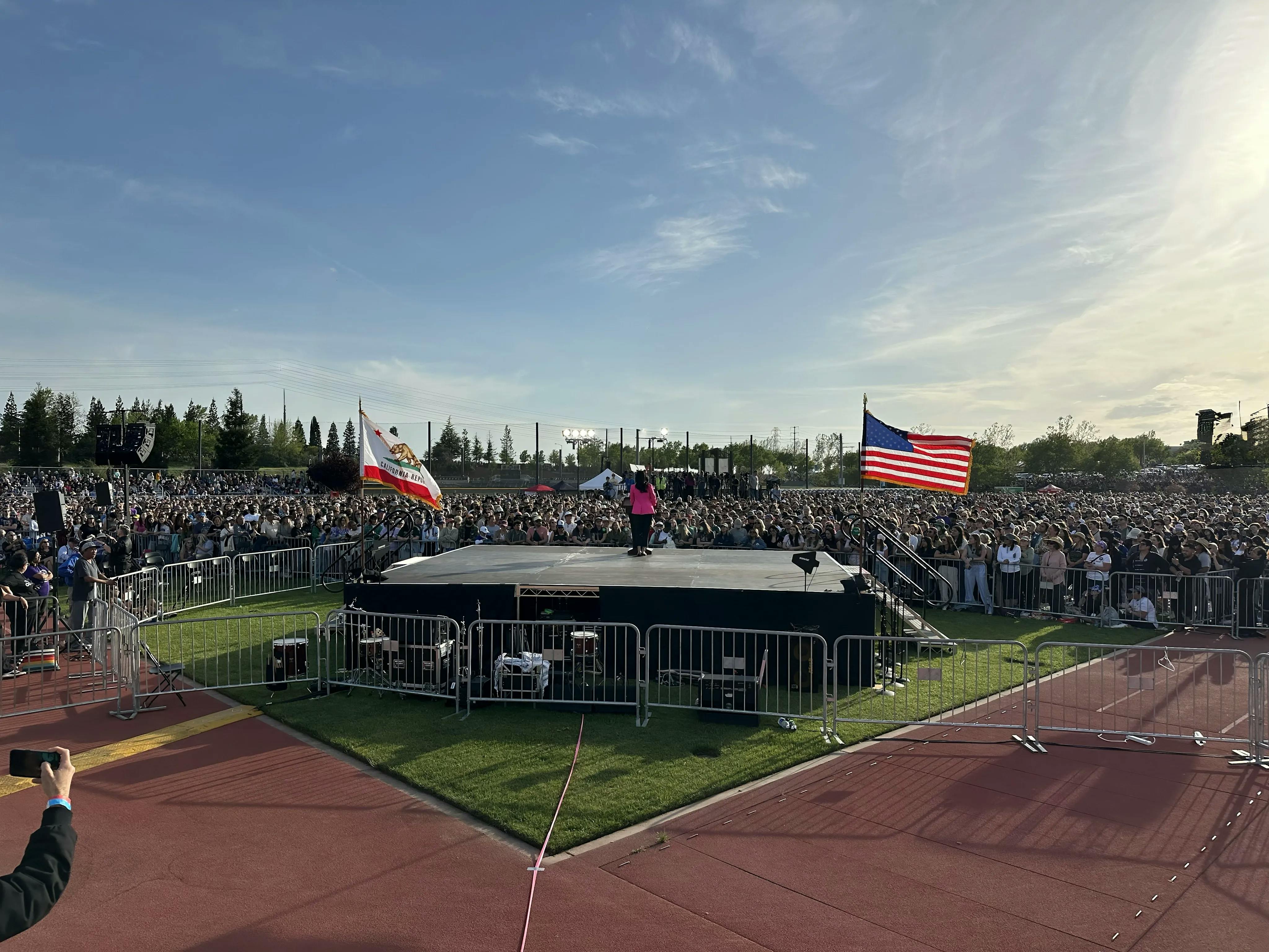 Jane Kim stands on stage in a pink blazer, speaker to a crowd of tens of thousands of people. To her left is the California state flag, and to her right the American flag.