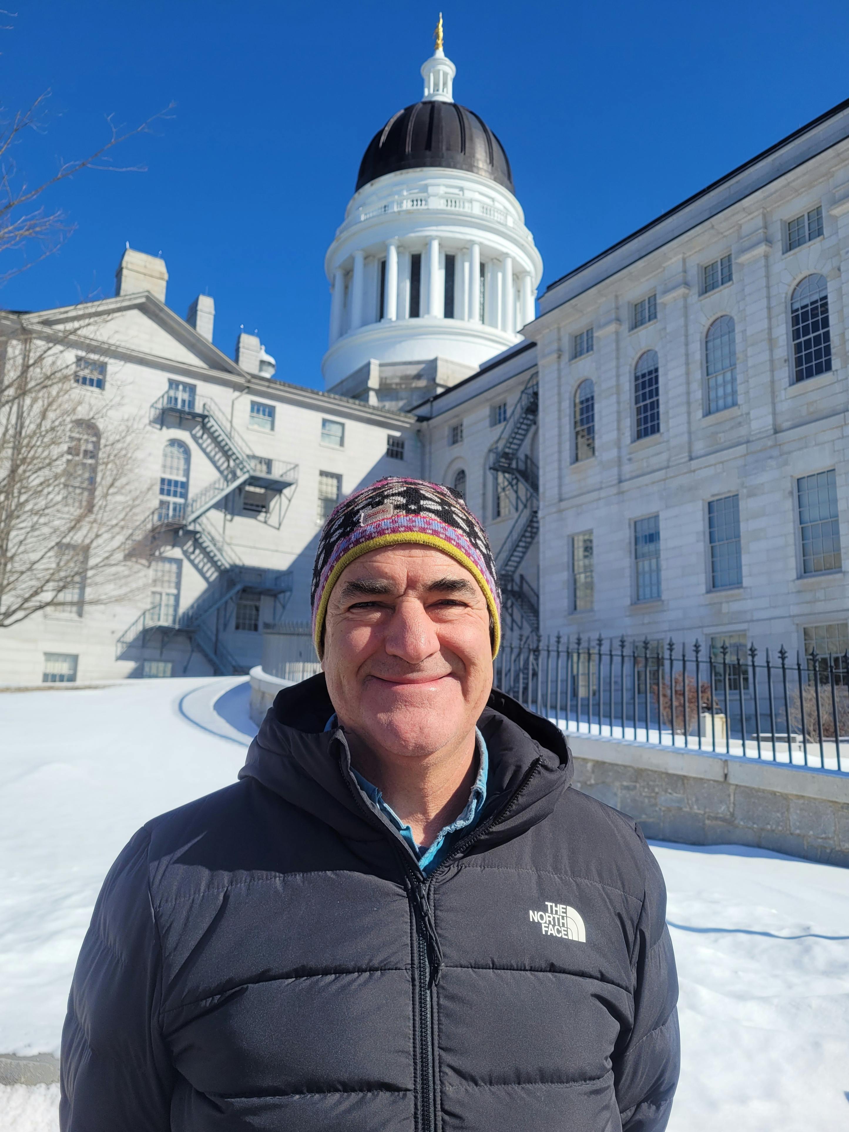 Portrait of candidate smiling in front of the Maine state Capitol