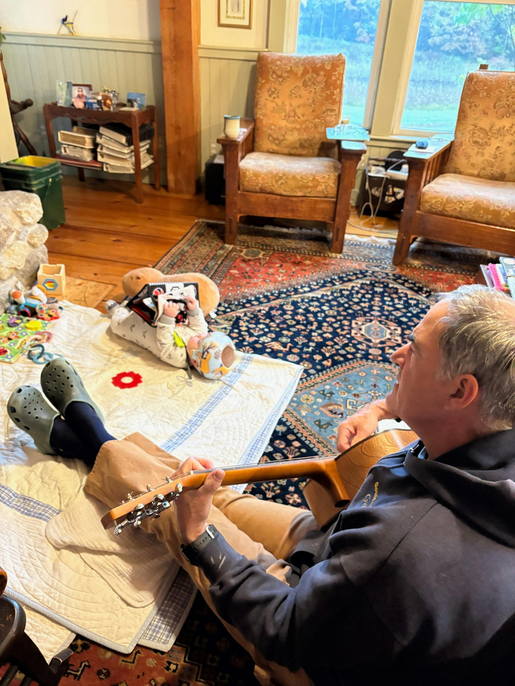 Candidate sitting on living room floor and playing guitar with baby
