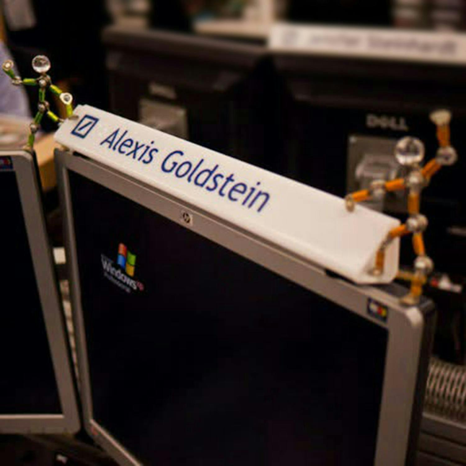 Una placa con el nombre que dice "Alexis Goldstein" sobre dos monitores de ordenador