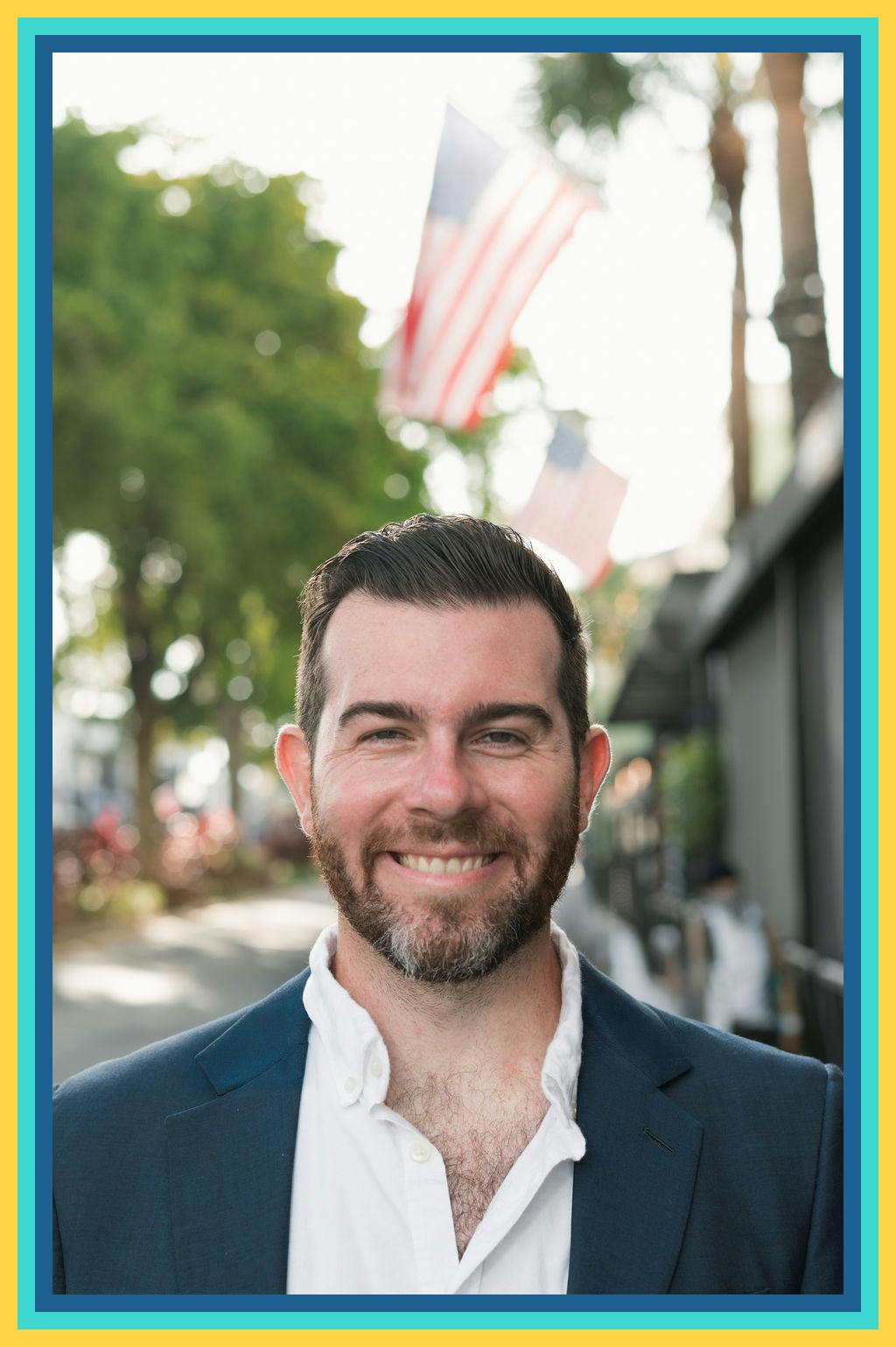  A man, candidate Oliver Larkin for FL-23, in a suit and tie smiles confidently in front of an American flag