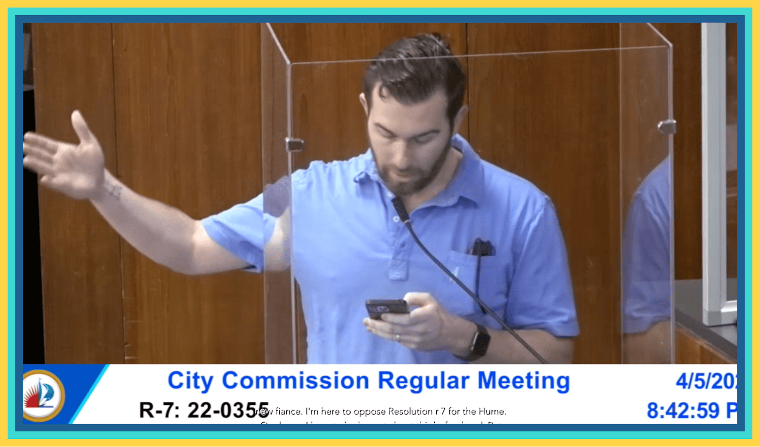 A man, Oliver Larkin, stands at a podium giving a speech during a city commission meeting.