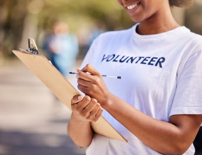Woman wearing a white tee shirt with the word volunteer on it, holding a pen and clipboard