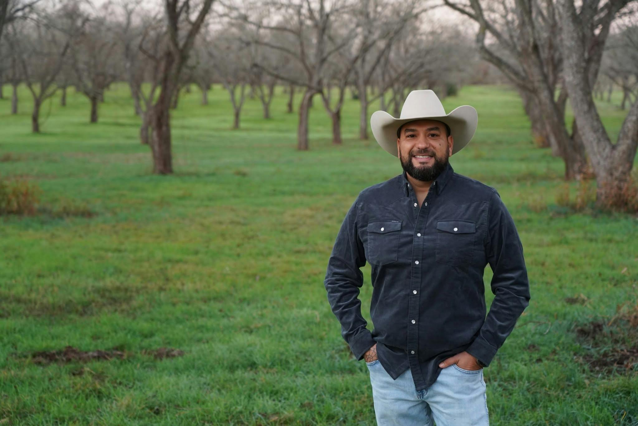 Chris Jimenez, Democratic candidate for Texas House District 52, standing in a pecan orchard on his family's farm in Williamson County