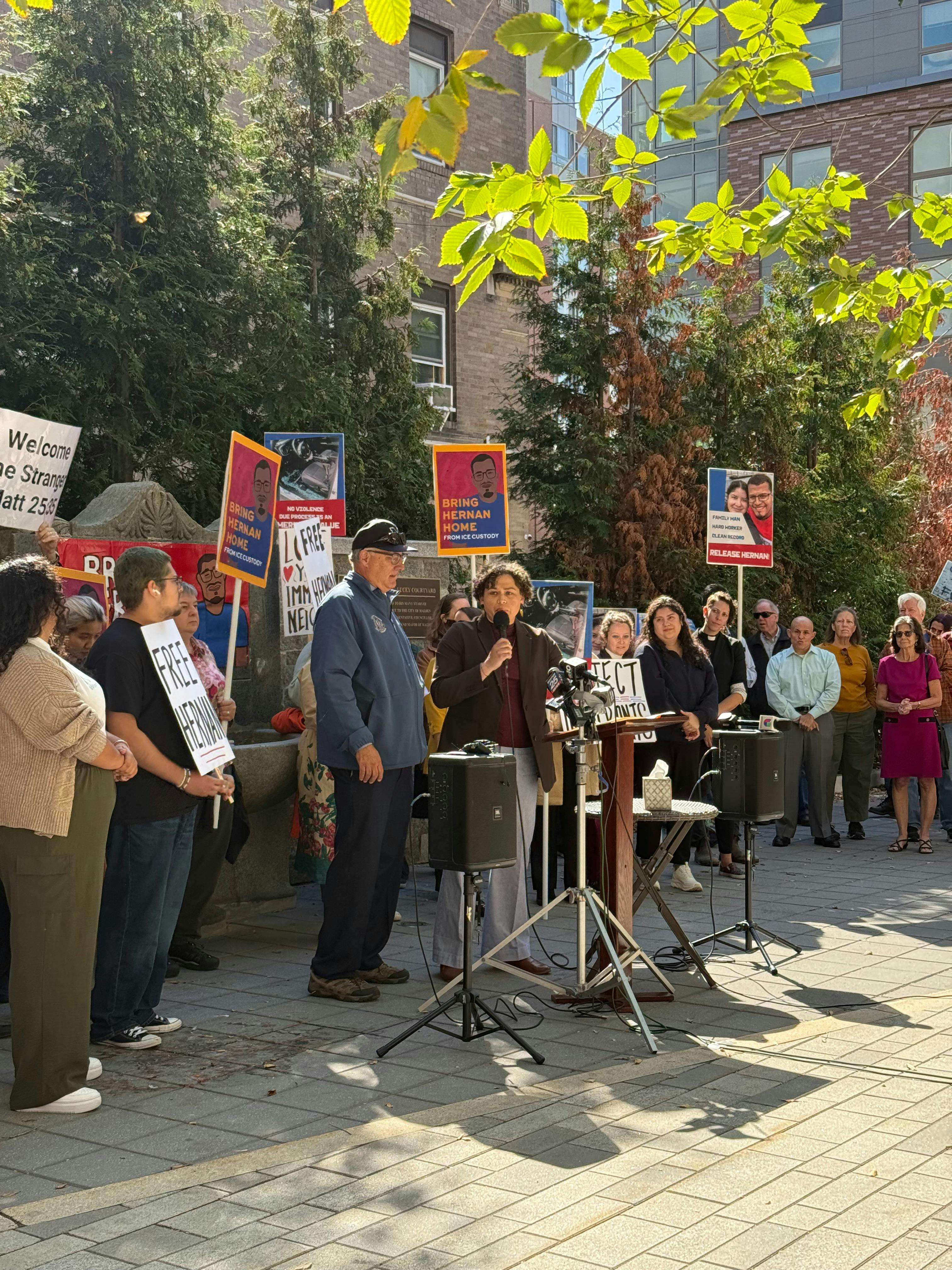 Carey is standing at a rally for a community members' release from immigration detention, in front of a crowd holding signs