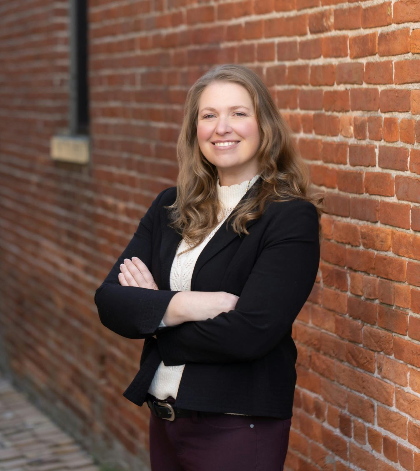 Katie Clendaniel standing confidently with arms crossed beside a brick wall