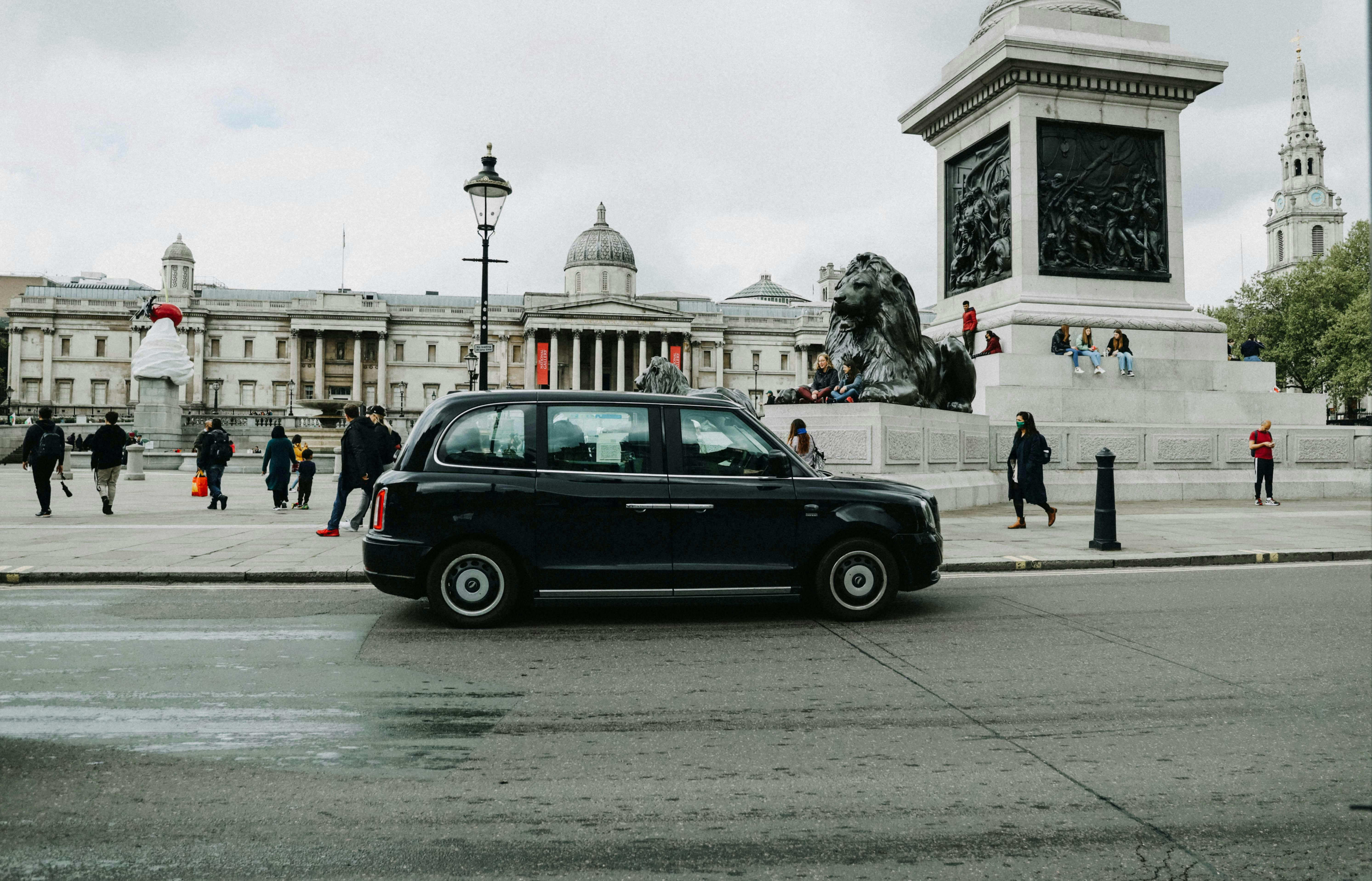 Photograph of a black cab taxi driving through Trafalgar Square