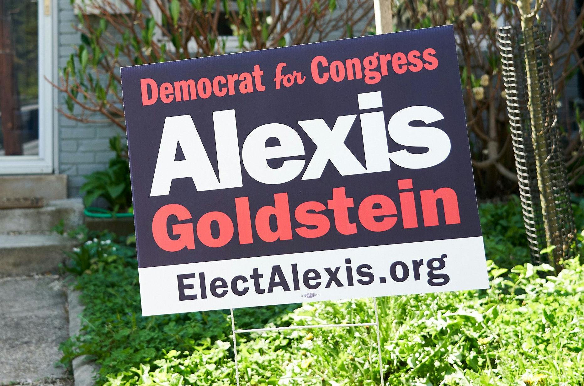 picture of a blue, white, and pink yard sign that reads "Democrat for Congress: Alexis Goldstein, ElectAlexis.org" and a union bug, showing the sign was union-printed.