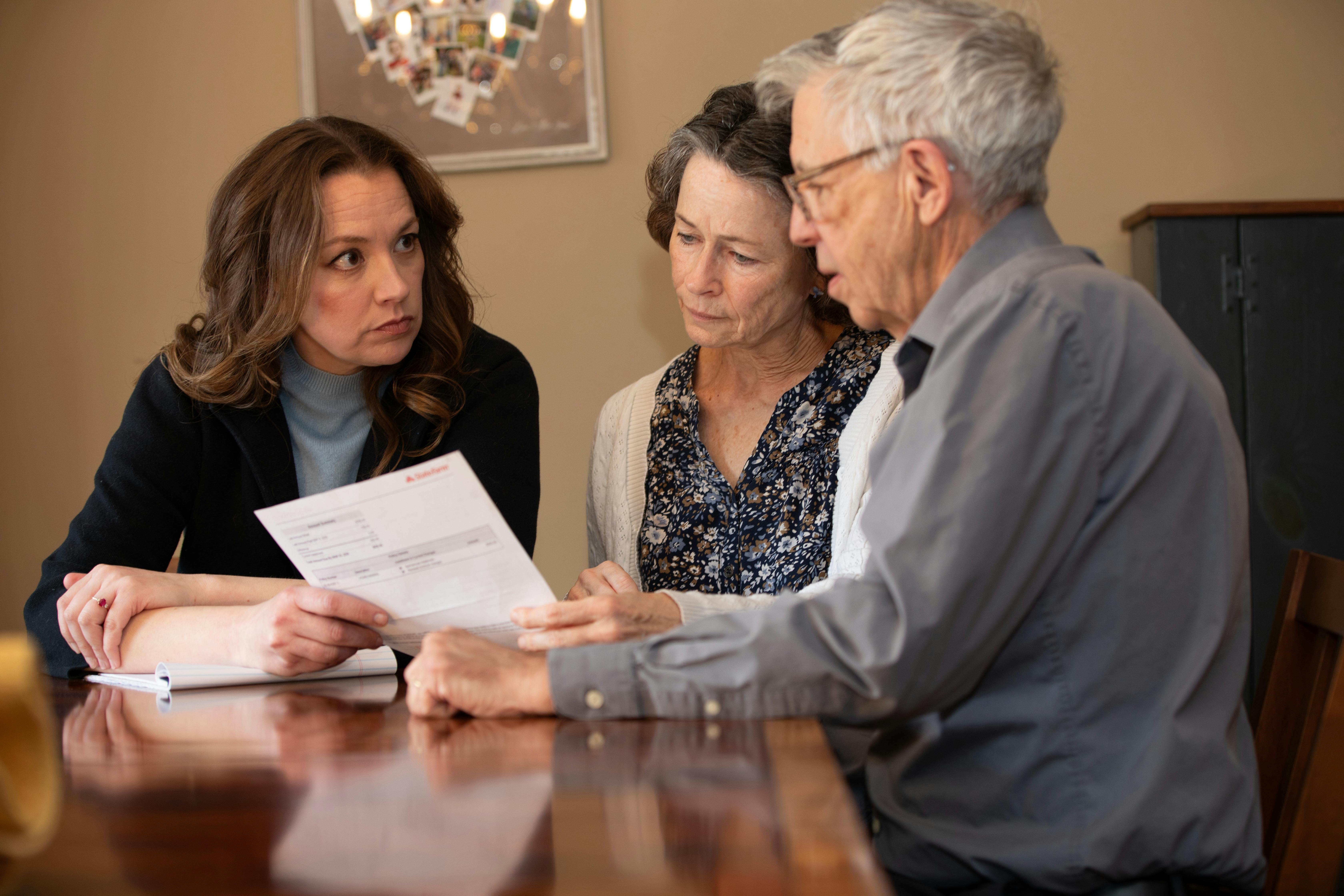 Sarah at kitchen table with an elder couple, looking at an insurance bill